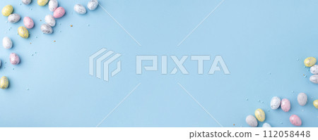 Festive Easter background. Multicoloured Easter eggs on a blue table. Banner with a place for text. Top view. 112058448