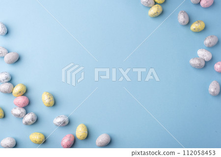 Festive Easter background. Multicoloured Easter eggs on a blue table. Card with a place for text. Top view. Festive Easter background. Multicoloured Easter eggs on a blue table. Card with a place for text. Top view. 112058453