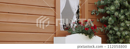 Banner bright red flowers in a window flowerbed of a wooden house Banner bright red flowers in a window flowerbed of a wooden house 112058800