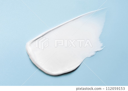 White smear of cream, mask or balm on a blue background. The texture of the skin or hair care product. White smear of cream, mask or balm on a blue background. The texture of the skin or hair care product. 112059153