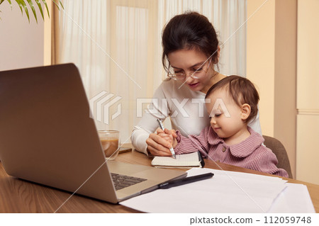 Cheerful pretty businesswoman working on laptop at home with her little child girl. mom spending time with her cute baby 112059748