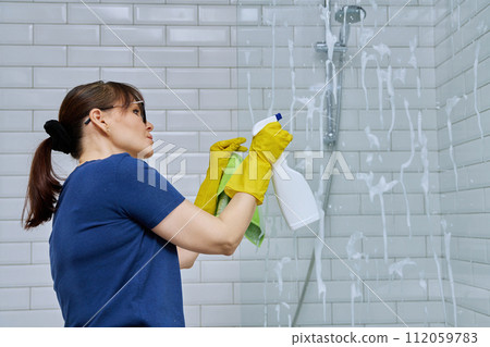 Woman cleaning bathroom, washing glass in shower Woman cleaning bathroom, washing glass in shower 112059783