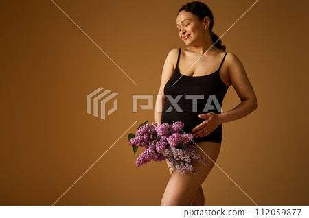 Pregnant woman with big belly in last pregnancy trimester, in black lingerie, holding lilacs, isolated beige backdrop Pregnant woman with big belly in last pregnancy trimester, in black lingerie, holding lilacs, isolated beige backdrop 112059877