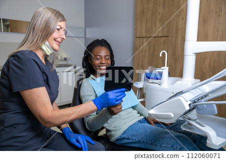 Multiracial woman sitting in chair In stomatology cabinet looking at mirror at her perfect smile Multiracial woman sitting in chair In stomatology cabinet looking at mirror at her perfect smile 112060071