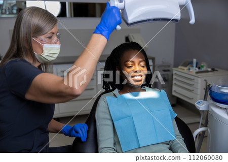 Female dentist examining woman patient with tools in dental clinic getting dental treatment 112060080