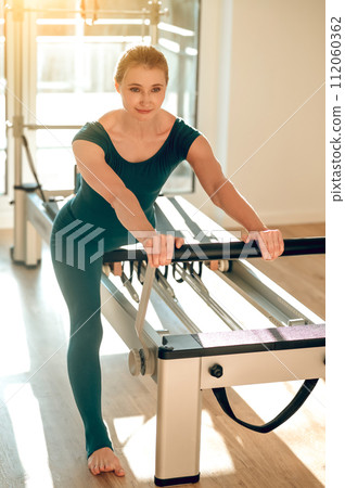 Female using Pilates reformer doing exercises training flexibility and muscle strength 112060362