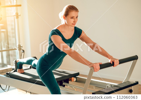 Woman doing exercises for muscular activity and body health on simulator in Pilates studio 112060363