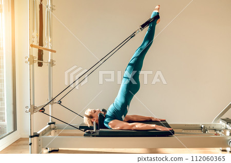 Woman doing exercises for muscular activity and body health on simulator in Pilates studio 112060365