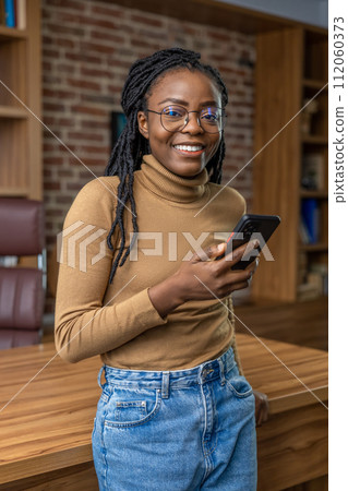 Woman with dreadlocks using mobile phone while standing in office 112060373