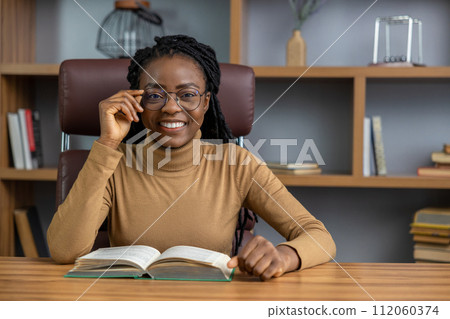 Smiling woman reading business book of entrepreneurship gaining insights for her business Smiling woman reading business book of entrepreneurship gaining insights for her business 112060374
