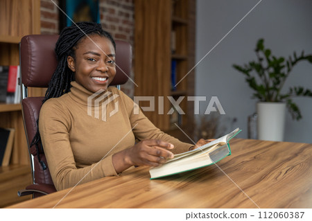 Woman sitting at table reading book student deepening her knowledge for educational purposes Woman sitting at table reading book student deepening her knowledge for educational purposes 112060387