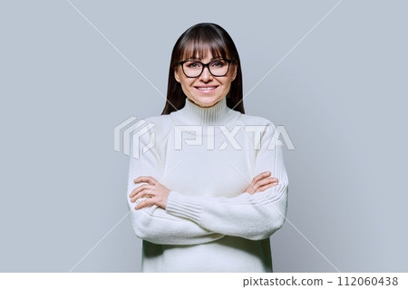 Middle-aged beautiful smiling woman in white sweater on gray studio background 112060438