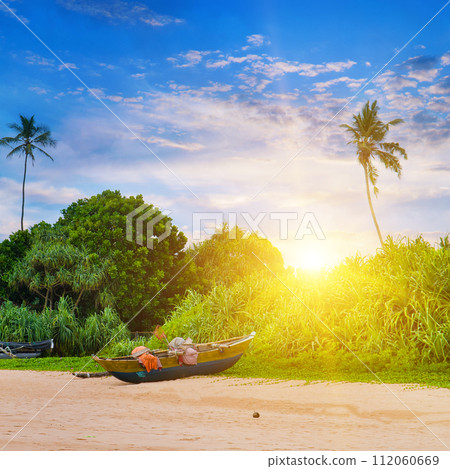 Wooden fishing boats on the sandy beach. Tropical landscape with palm trees and bright sun set. Sri Lanka. 112060669