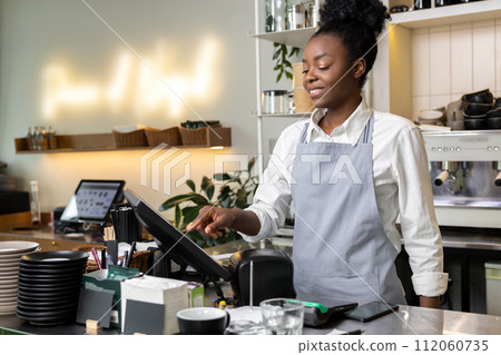 Multicultural woman waiter standing at cafe counter using terminal Multicultural woman waiter standing at cafe counter using terminal 112060735
