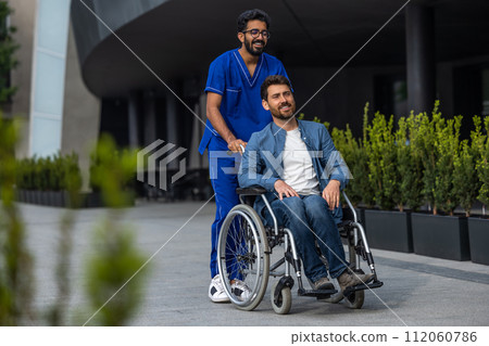 Brunette man in doctors overall carrying a wheelchair with a patient Brunette man in doctors overall carrying a wheelchair with a patient 112060786
