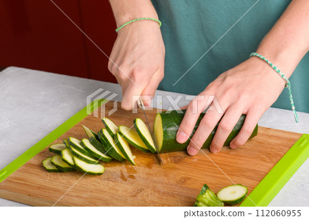 Woman's hands cutting zucchini on wooden cutting board at home, preparing healthy food, close up 112060955