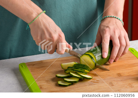 Woman's hands cutting zucchini on wooden cutting board at home, preparing healthy food, close up 112060956