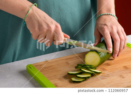 Woman's hands cutting zucchini on wooden cutting board at home, preparing healthy food, close up 112060957
