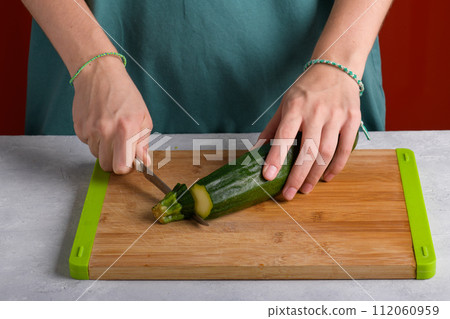 Woman's hands cutting zucchini on wooden cutting board at home, preparing healthy food, close up 112060959