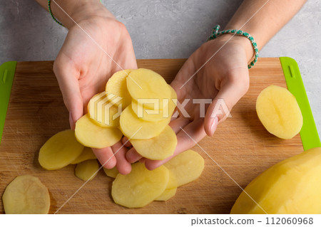 Authentic female hands holding cutting potatoes on wooden cutting board on kitchen table background 112060968