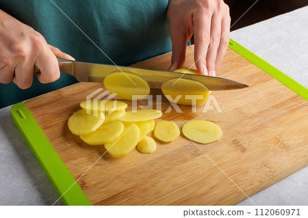 Authentic female hands cutting potatoes on wooden cutting board on gray kitchen table 112060971
