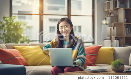 smiling chineese girl in colorful casual clothes working at a laptop at home, beige sofa, modern room space 112061331