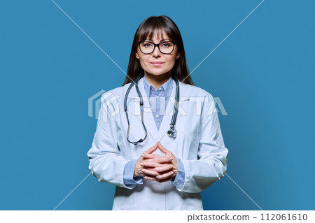 Confident friendly female doctor looking at camera on blue background 112061610