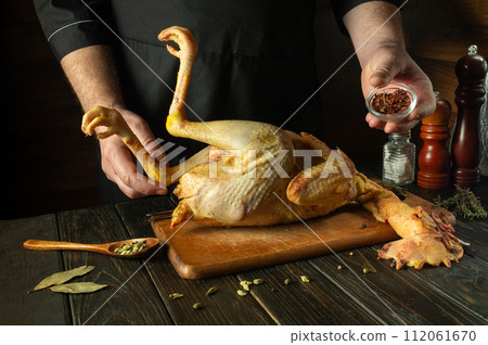 Chef preparing raw rooster in the kitchen. Before frying, the cook adds spices to the rooster. Preparing to cook fried poultry in the inn kitchen 112061670