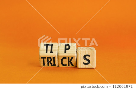 Tips and tricks symbol. Turned wooden cubes and changed the word tricks to tips. Beautiful orange table, orange background. Business, tips and tricks concept. Copy space. 112061971