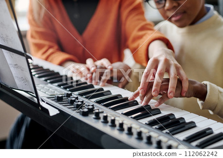 Selective focus shot of unrecognizable woman teaching Black boy to play synthesizer at music class Selective focus shot of unrecognizable woman teaching Black boy to play synthesizer at music class 112062242