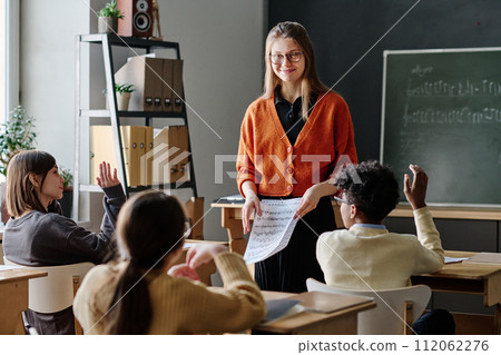 Selective focus medium long shot of cheerful young Caucasian woman conducting music class at school Selective focus medium long shot of cheerful young Caucasian woman conducting music class at school 112062276