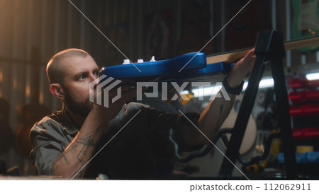 Male carpenter inspects guitar and wipes strings with rag 112062911