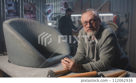 Professional male carpenter stands near chair and looks at camera 112062916