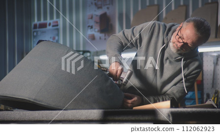 Mature craftsman changes chair upholstery using staple gun Mature craftsman changes chair upholstery using staple gun 112062923