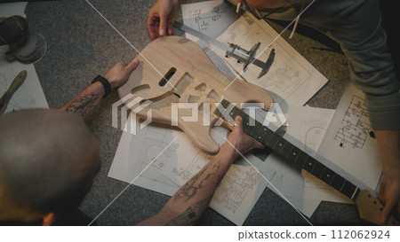 Top view of two male carpenters making guitar in workshop Top view of two male carpenters making guitar in workshop 112062924