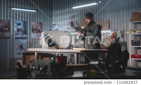 Male designer takes photo of chair using tablet computer in furniture workshop 112062937