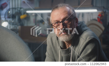 Professional mature craftsman in glasses looks at camera 112062943