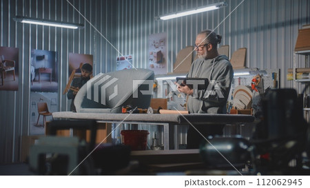 Mature carpenter or designer uses digital tablet in furniture workshop 112062945