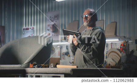 Mature carpenter or designer uses tablet computer creating or restoring chair 112062988