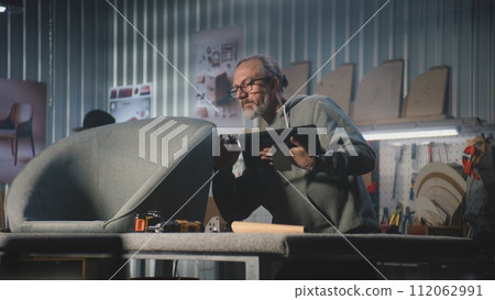 Mature carpenter or designer uses tablet computer creating or restoring chair 112062991