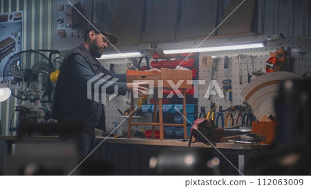 Male carpenter assembles bedside table working in furniture workshop 112063009
