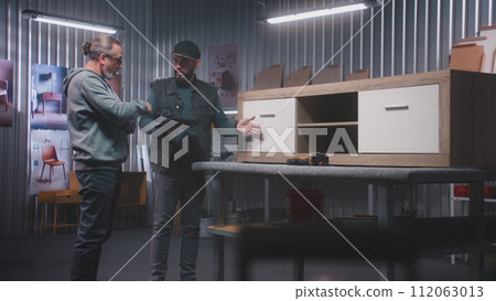 Male designer with digital tablet discusses making TV stand with colleague 112063013