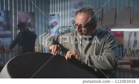 Mature carpenter makes upholstery of chair using staple gun Mature carpenter makes upholstery of chair using staple gun 112063016