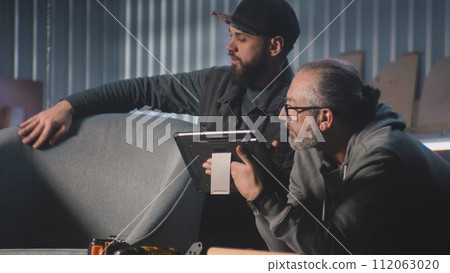Professional craftsmen discuss chair design and making using tablet computer 112063020