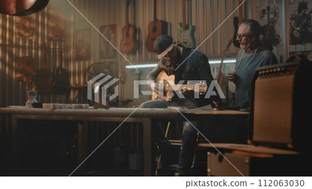 Mature music teacher teaches man to play on guitar in stylish garage studio Mature music teacher teaches man to play on guitar in stylish garage studio 112063030