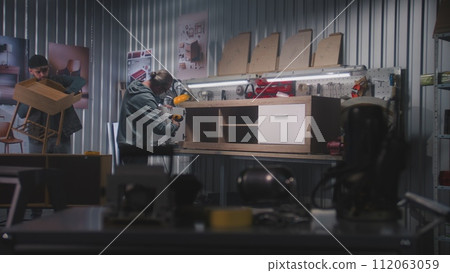 Mature carpenter assembles TV stand using screwdriver 112063059