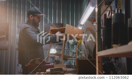 Male craftsman assembles wooden nightstand in furniture workshop Male craftsman assembles wooden nightstand in furniture workshop 112063062