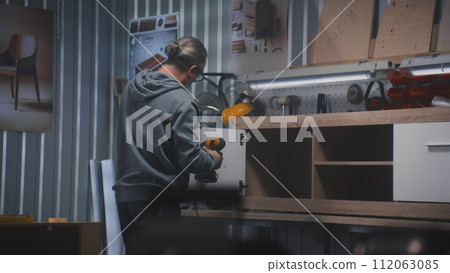 Professional male craftsman makes and assembles TV stand 112063085