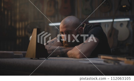 Tired carpenter looks at metronome, sits in workshop Tired carpenter looks at metronome, sits in workshop 112063105