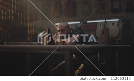 Tired carpenter looks at metronome, sits in workshop 112063113